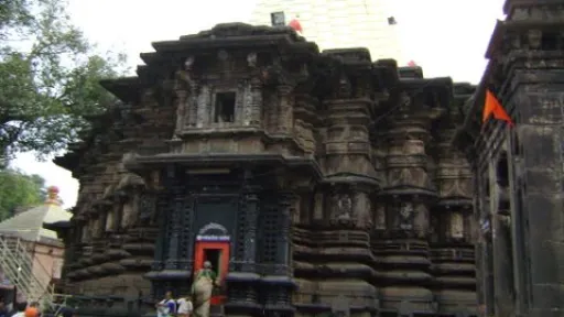 Intricately carved dark stone temple with a light spire, crowds of people gather below.