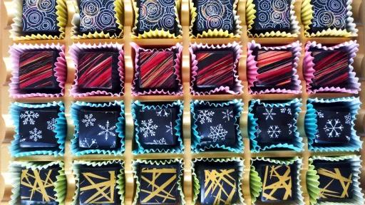 Assorted gourmet chocolates in a box, featuring swirls, stripes, snowflakes, and abstract gold lines.