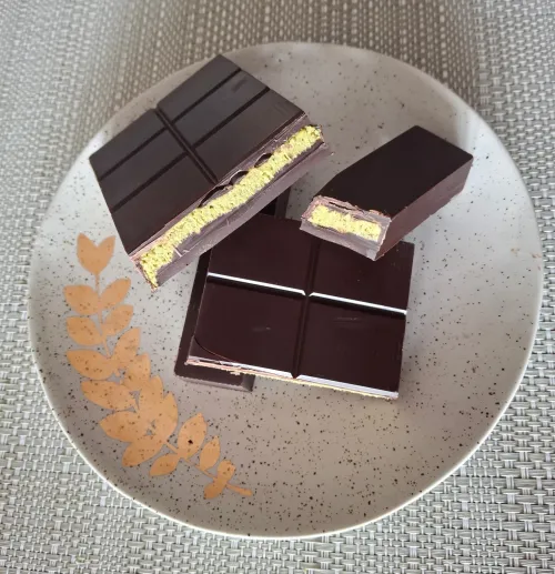 Dark chocolate pieces with creamy pistachio filling on a speckled plate.