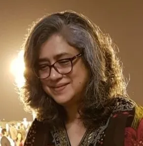 Nita with graying hair and glasses smiles, illuminated by a warm glow from the left.